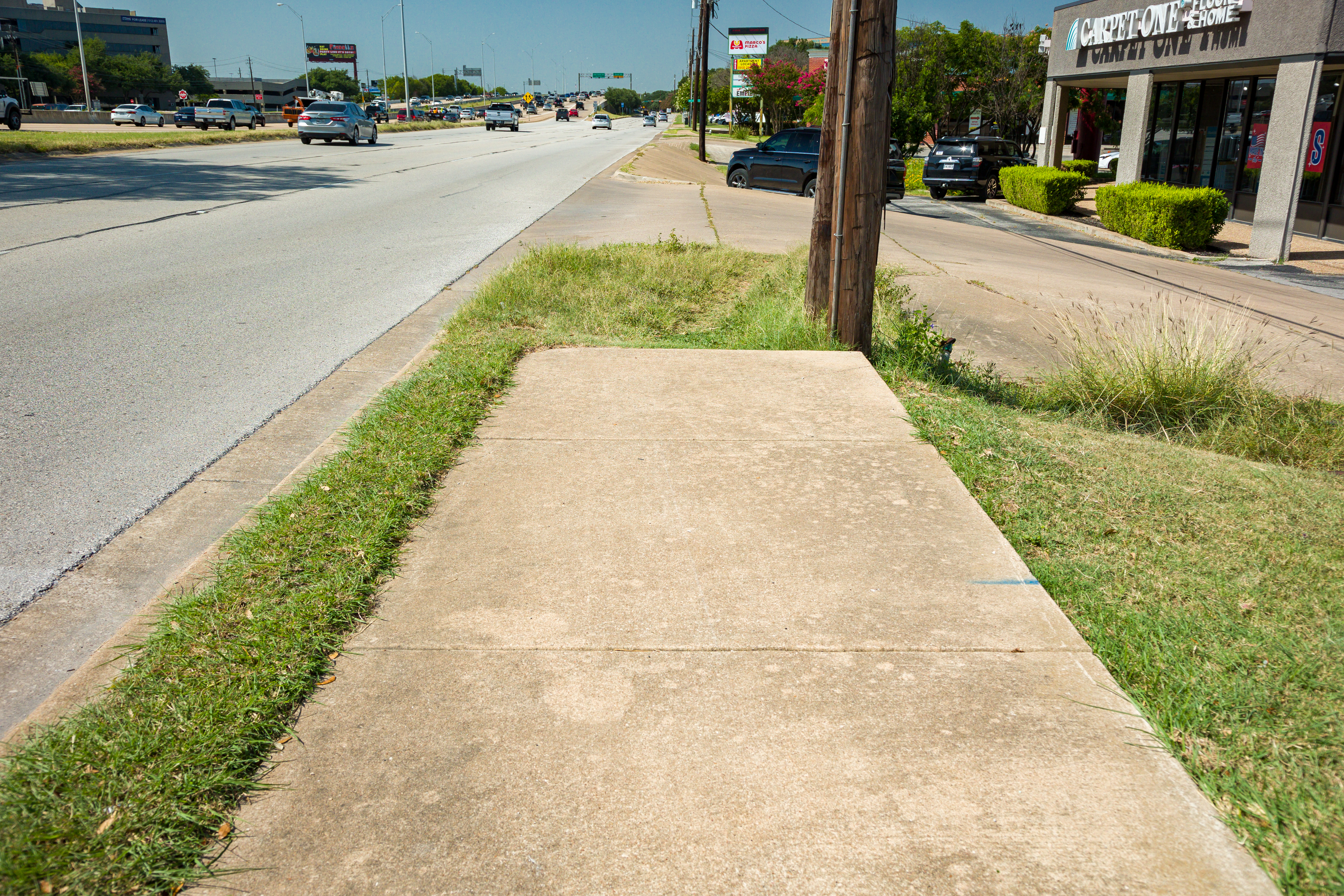 A discontinuous sidewalk and business driveway on the existing US 183 Frontage Roads.