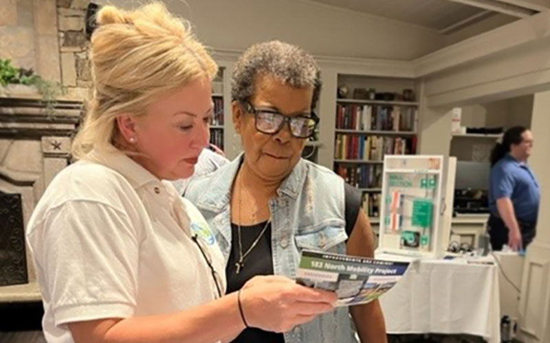 Two women stand together looking at a flyer that one of them is holding. 