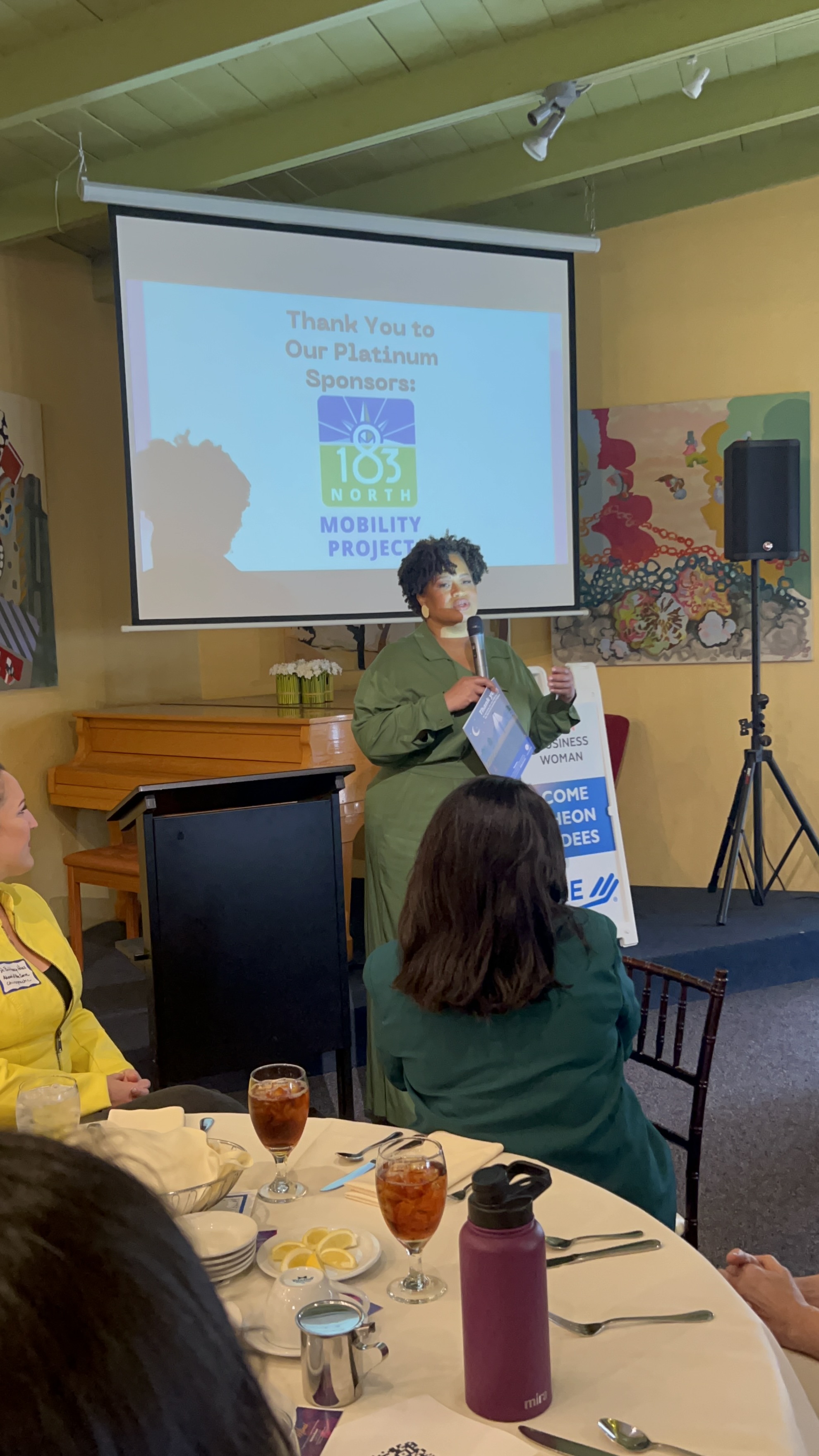 Woman speaks to group dining at luncheon tables