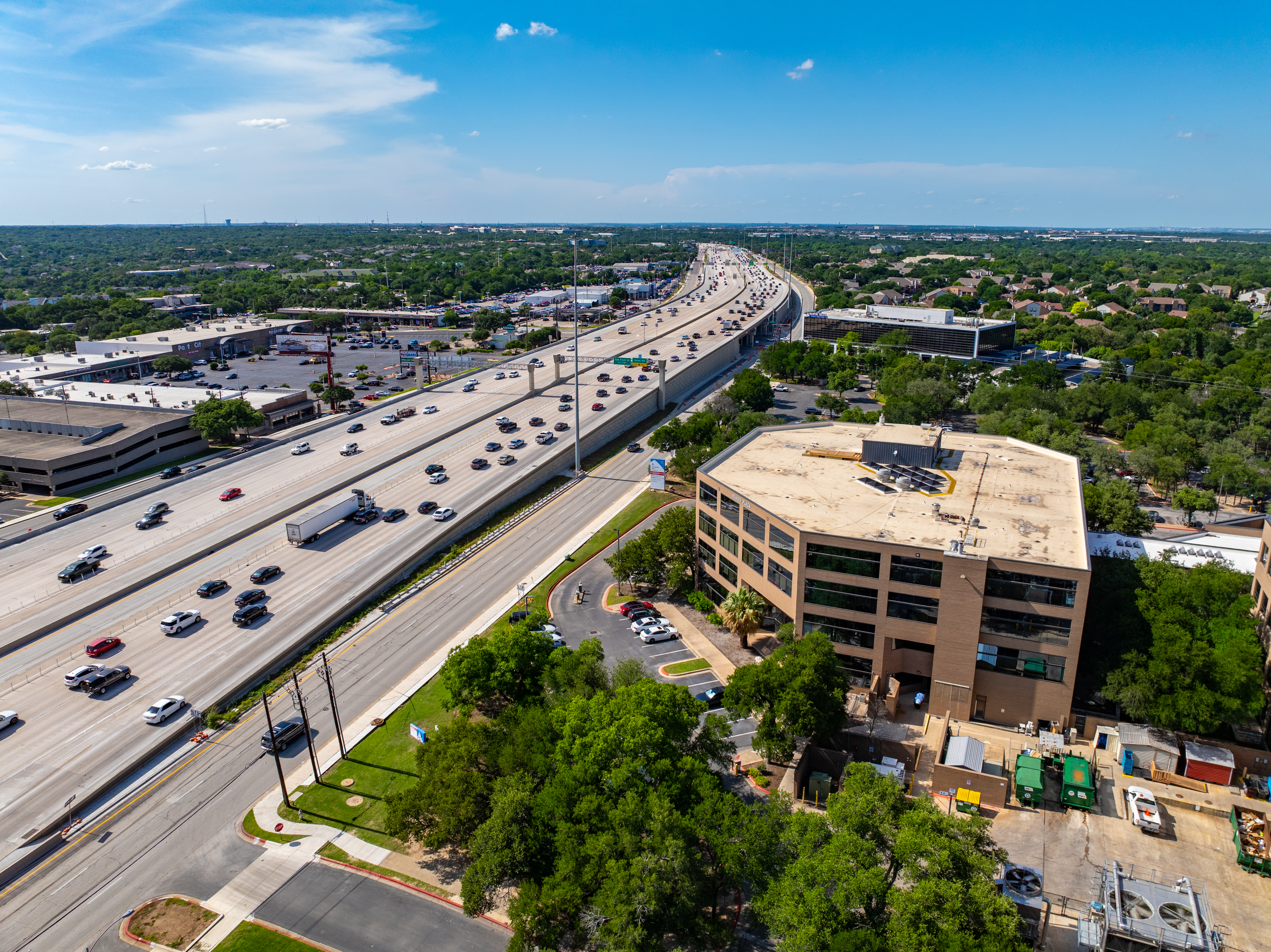 •	Right-angled aerial view of the 183 North Mobility Project near Ascension Seton Northwest Hospital, highlighting the northbound frontage road and entrance to the direct connector, with commercial buildings on one side of the roadway.