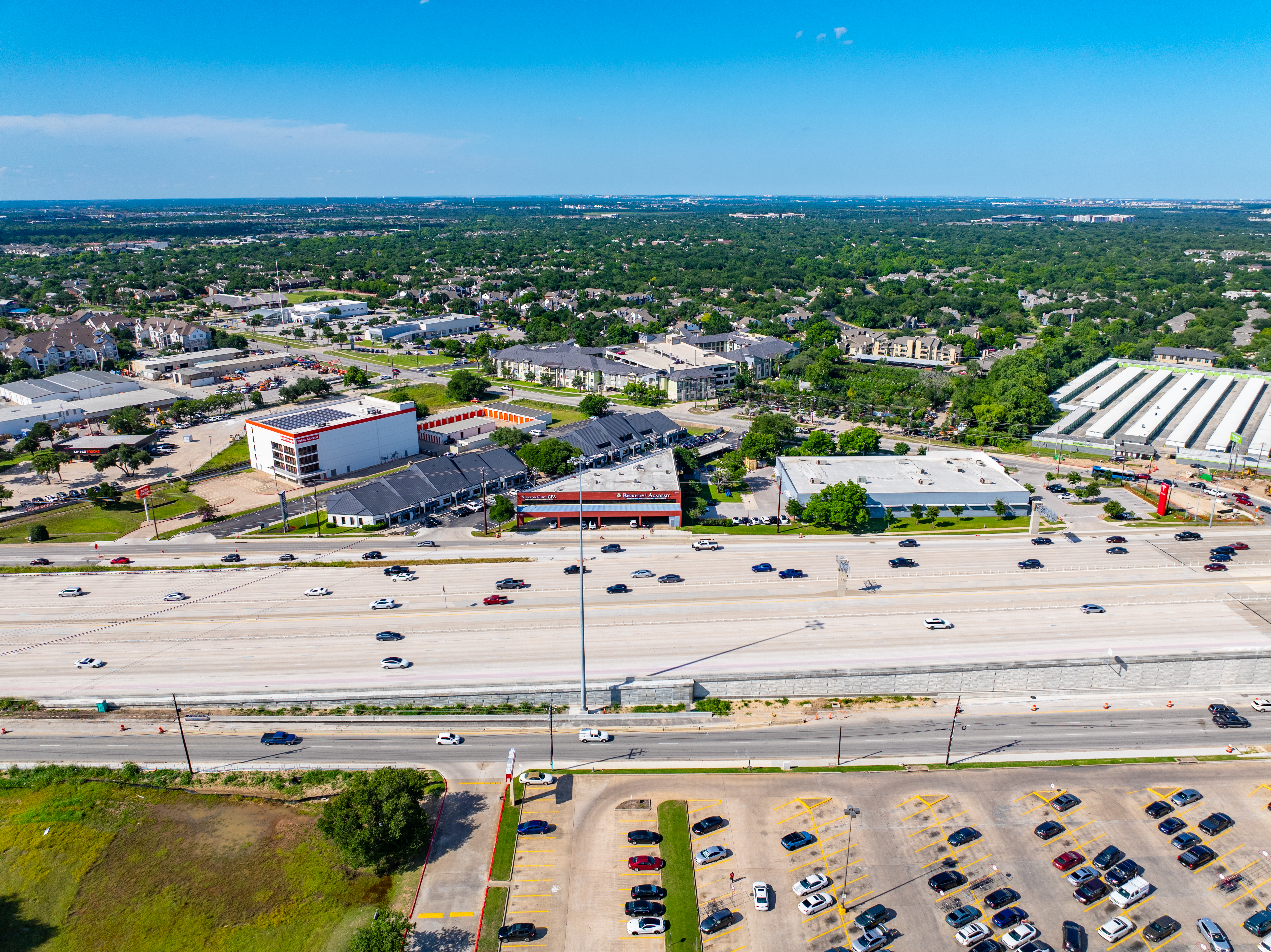 Aerial view facing the southbound frontage road at Anderson Mill Road, showing the southbound express lanes and mainlanes with a parking lot along the southbound side and commercial businesses lining the northbound frontage road.