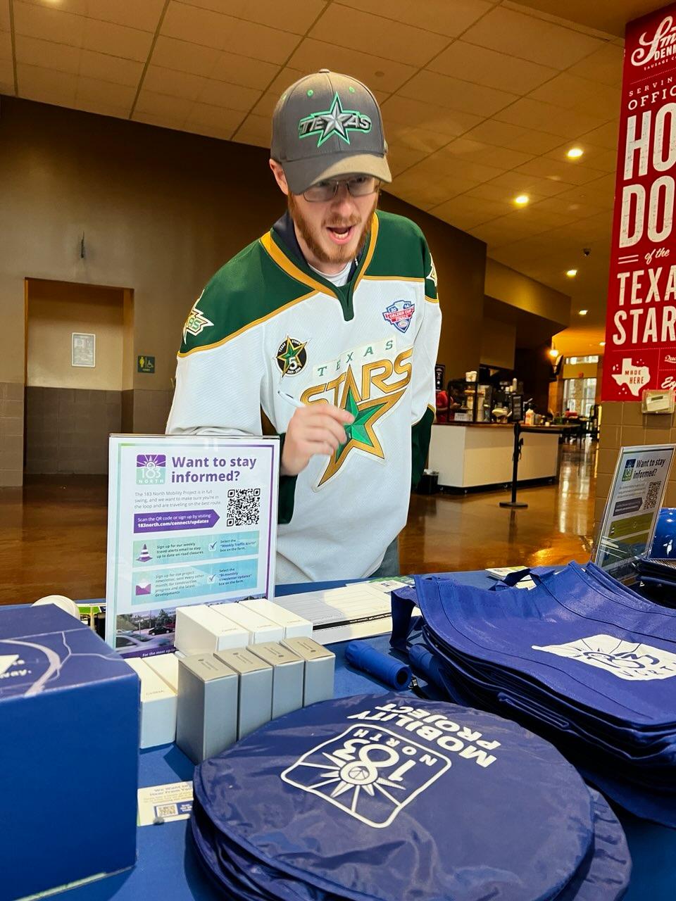 Man dressed in a hockey team jersey and hat visiting info table 